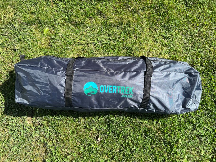 Handy carry bag A grey bag with black straps and a green logo, resting on green grass.