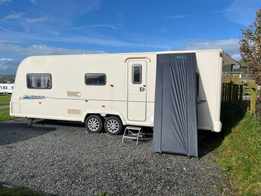 The Caravan Shed - front view A white caravan parked on gravel with a grey awning attached.